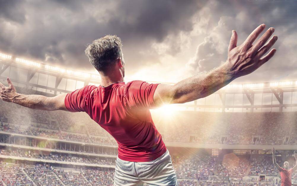 Ein Fußballspieler im roten Trikot jubelt mit dem Rücken zur Kamera nach einem Tor – perfekte Szene für alle, die auf „Beide Teams treffen“ (BTTS) gewettet haben.